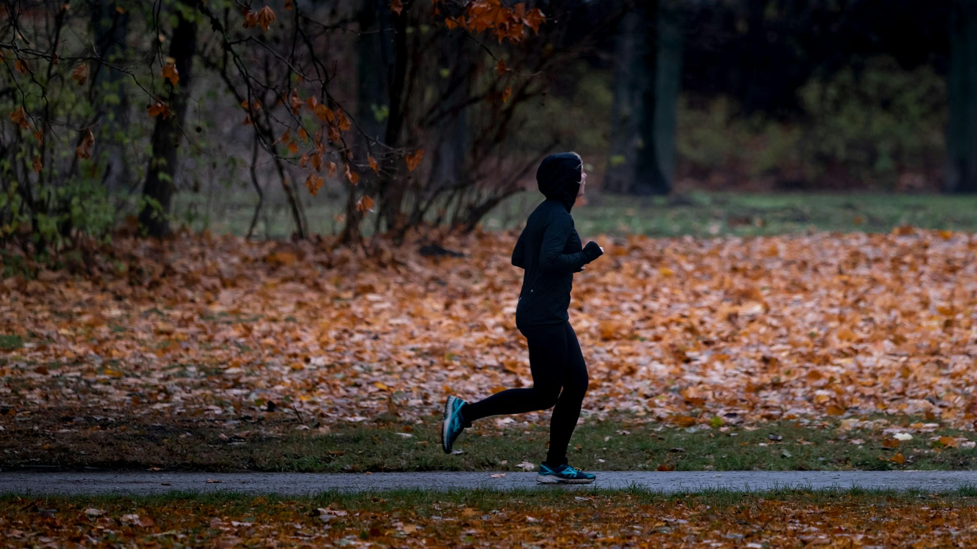 Eine Joggerin läuft bei Nieselregen durch einen Park.
