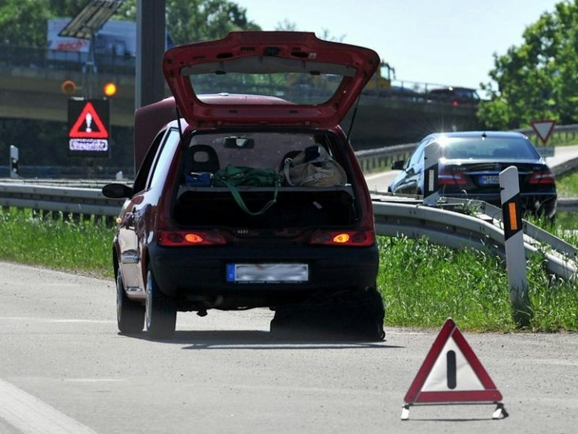 Ein Fahrzeug steht mit geöffnetem Kofferraum am Rand einer Autobahn, davor ein Warndreieck.