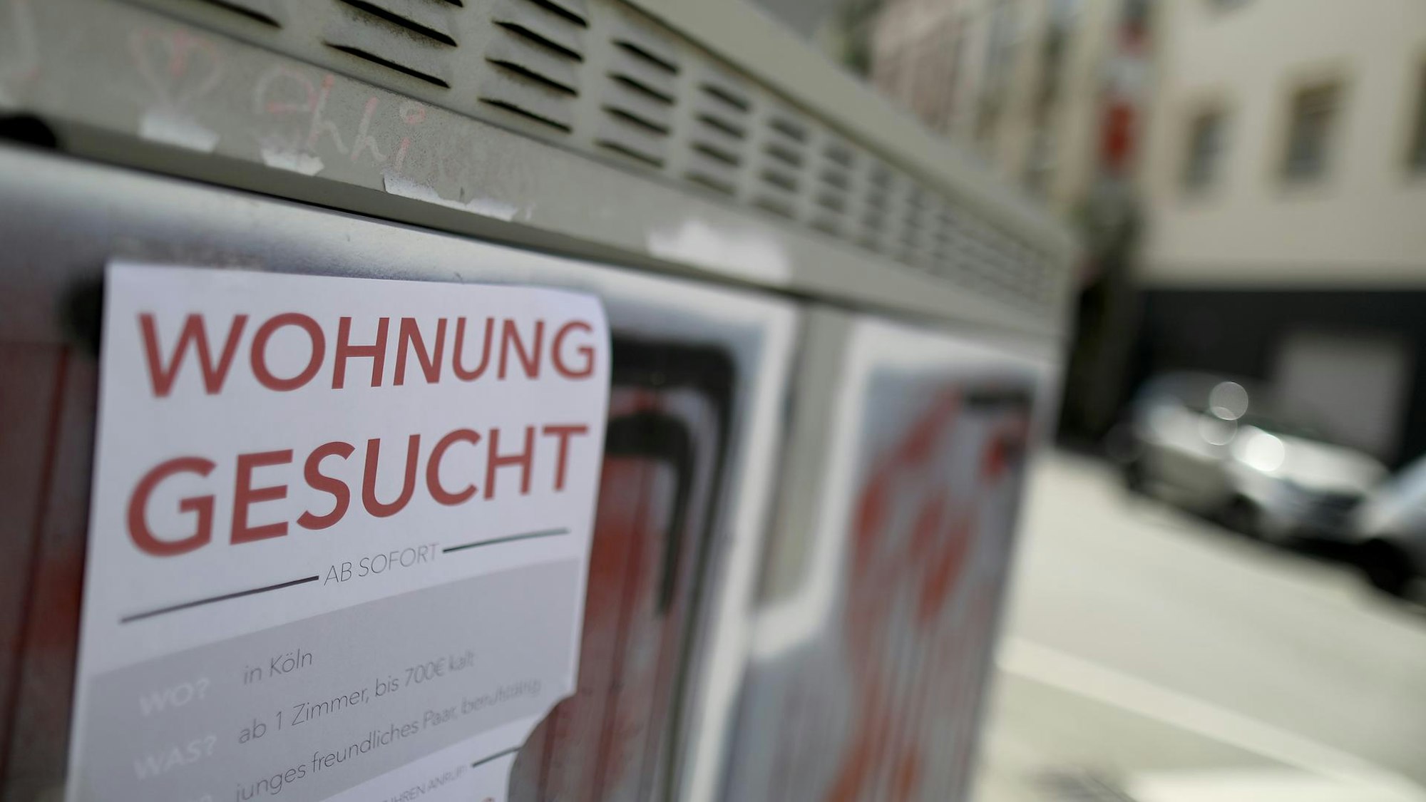 An einem Stromkasten hängt ein Zettel mit einem Wohnungsgesuch.