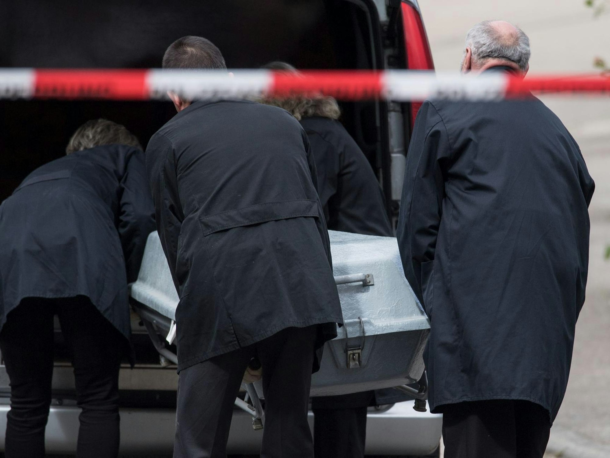 Bestatter schieben einen Zinksarg in den Leichenwagen.