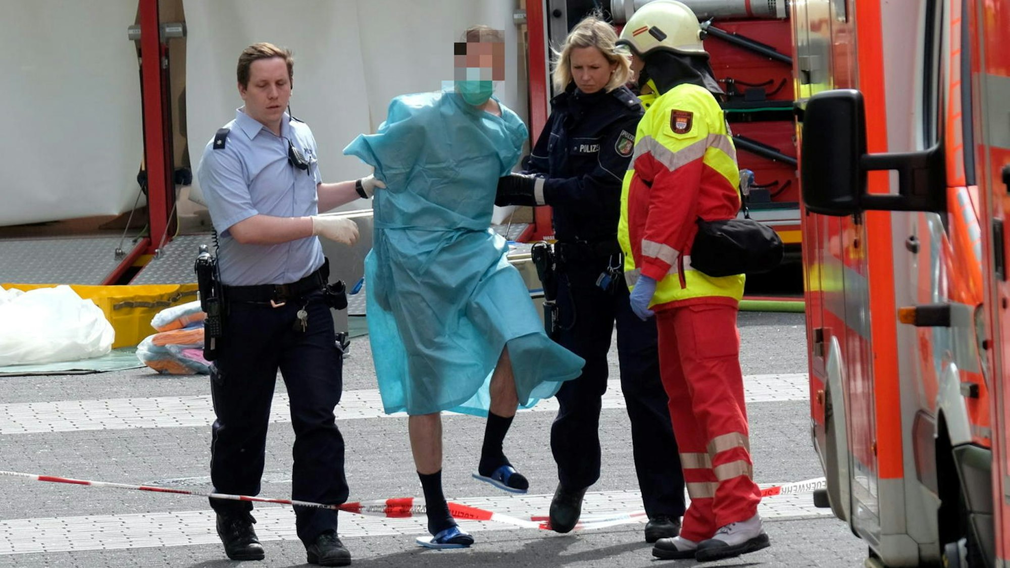 Ein Mann in einem blauen Kittel wird von Einsatzkräften abgeführt.