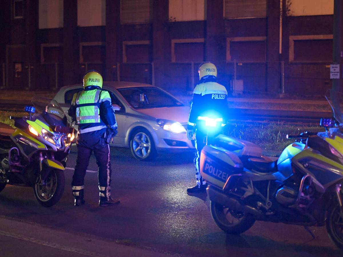 Zwei Polizisten stehen neben ihren Motorrädern und halten ein Auto an.