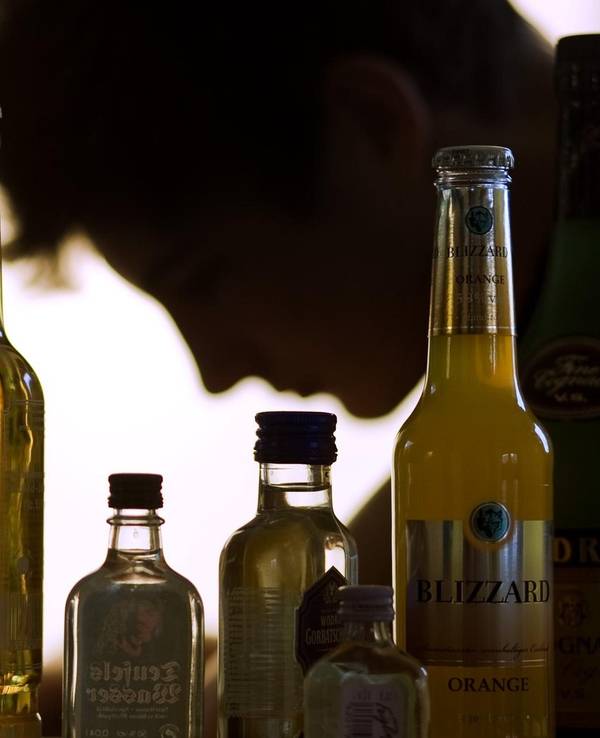 Flaschen mit Alkohol, darunter Bier und Whiskey, stehen aufgereiht vor einer Person, die nur im Profil zu sehen ist.