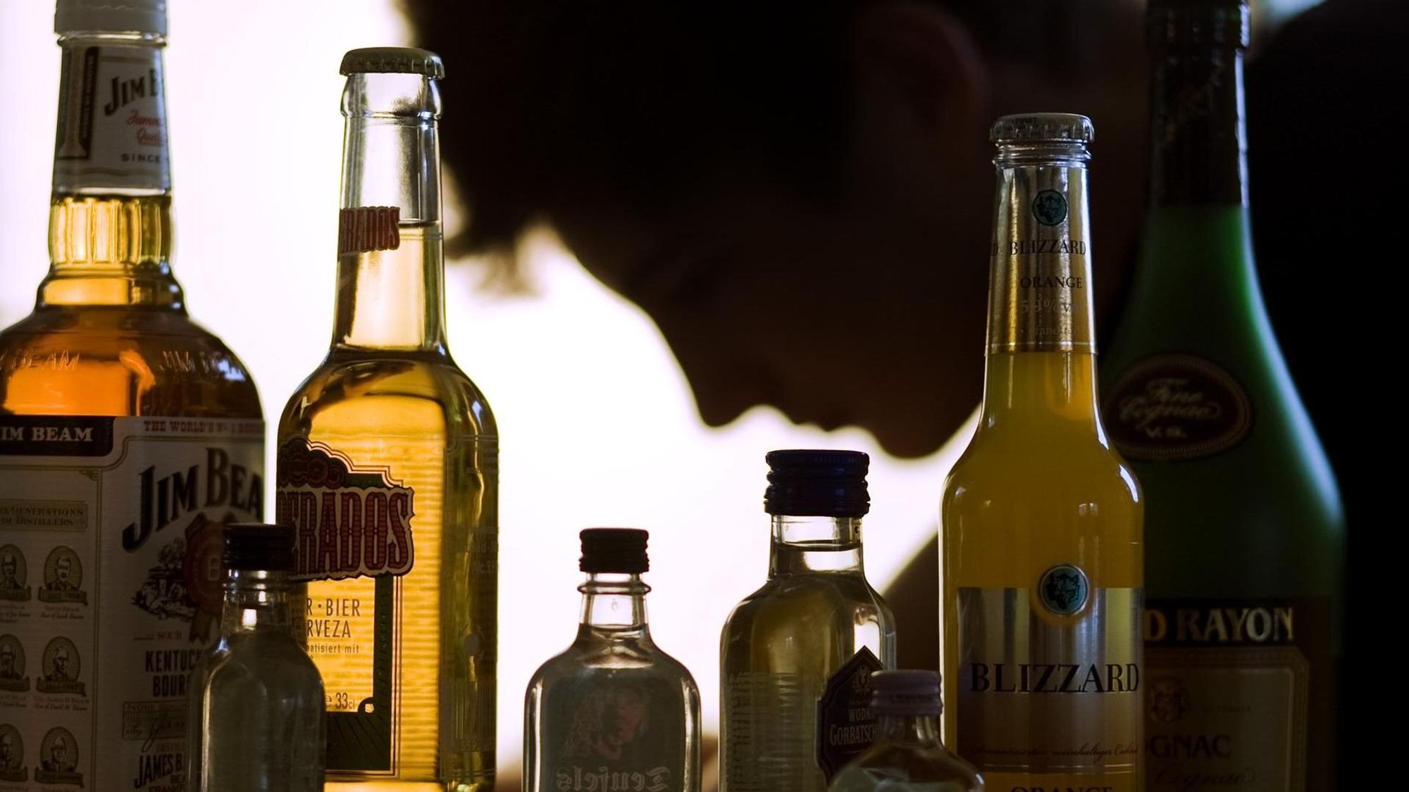 Flaschen mit Alkohol, darunter Bier und Whiskey, stehen aufgereiht vor einer Person, die nur im Profil zu sehen ist.