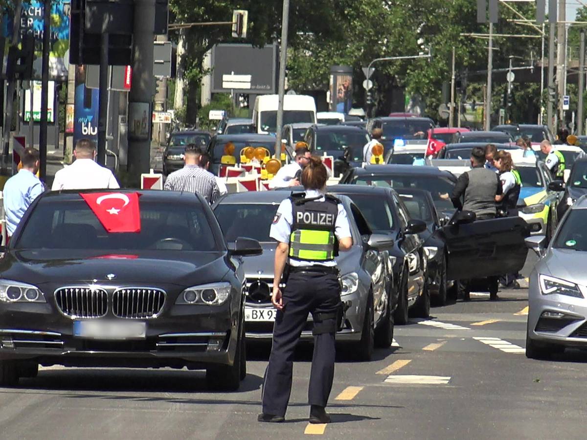Eine Polizistin steht vor einer Fahrzeugkolonne einer Hochzeitsgesellschaft.