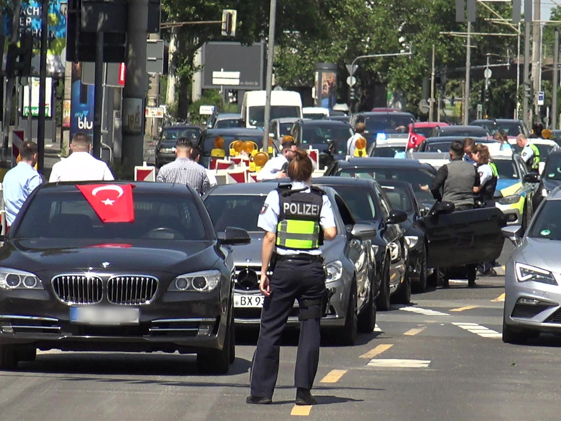 Eine Polizistin steht vor einer Fahrzeugkolonne einer Hochzeitsgesellschaft.