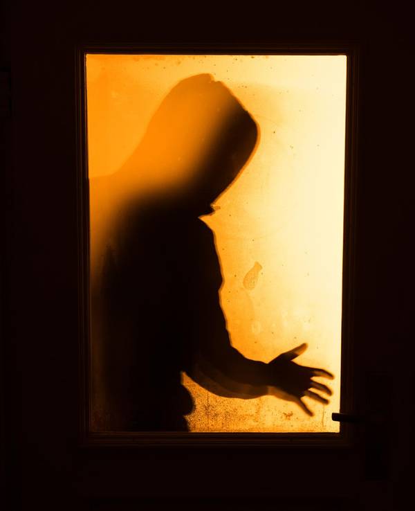 Durch eine Türscheibe ist der Schatten einer Person zu sehen.