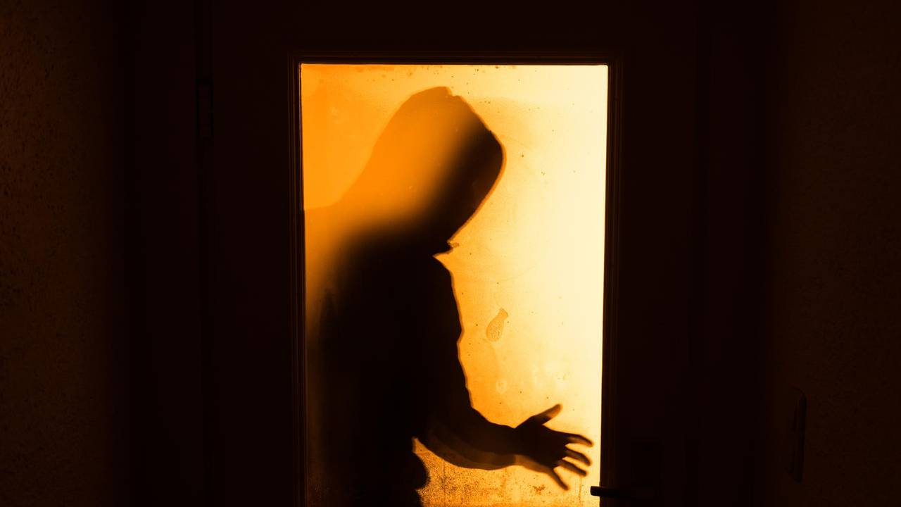 Durch eine Türscheibe ist der Schatten einer Person zu sehen.