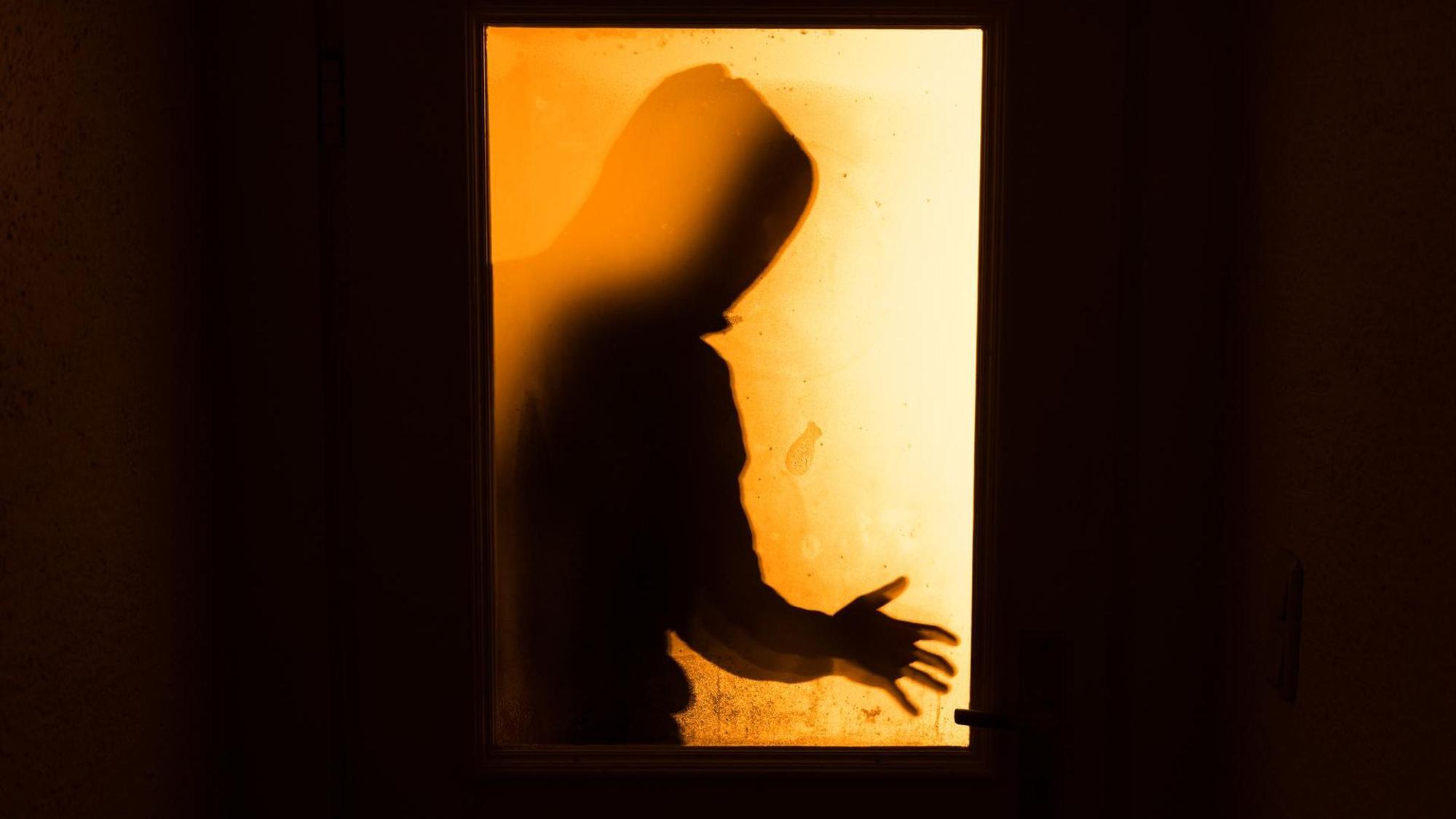 Durch eine Türscheibe ist der Schatten einer Person zu sehen.
