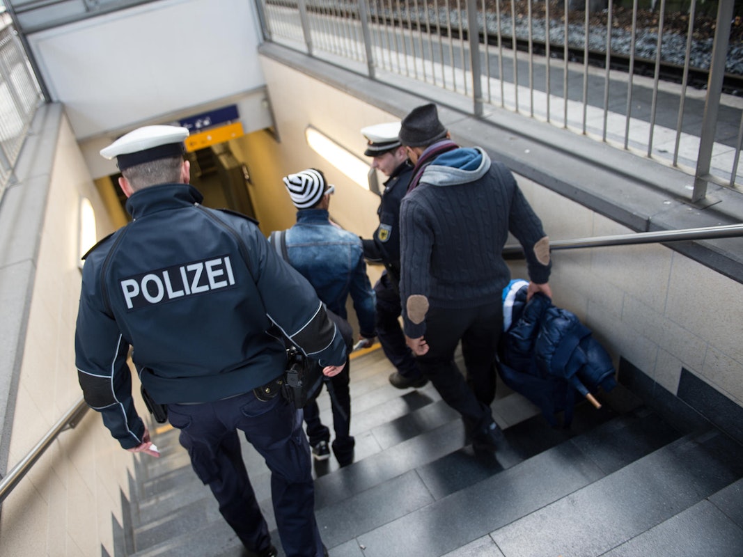 Zwei Polizisten gehen gemeinsam mit zwei Männern eine Treppe im Kölner Hauptbahnhof runter.