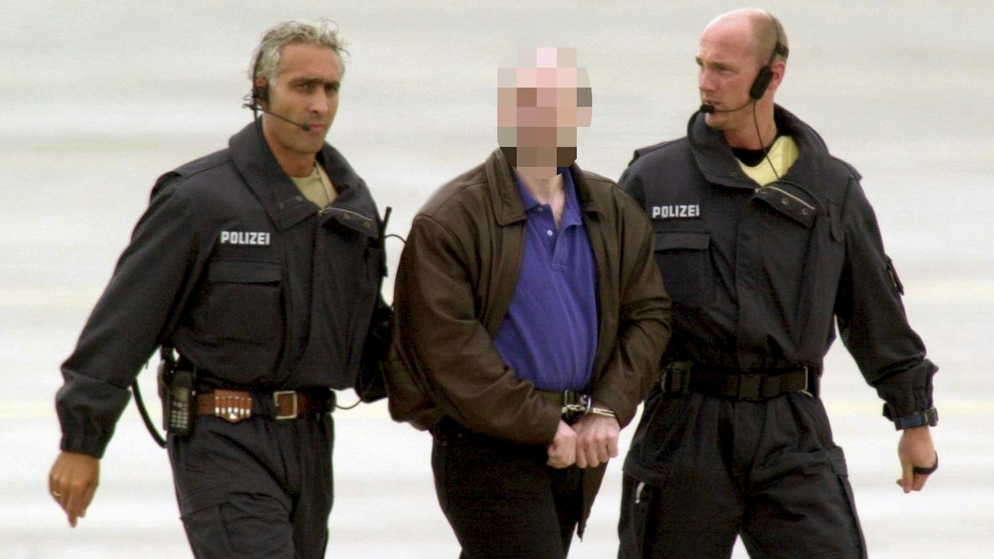 Der mit Handschellen gefesselte Thomas Drach wird von zwei Polizisten begleitet.