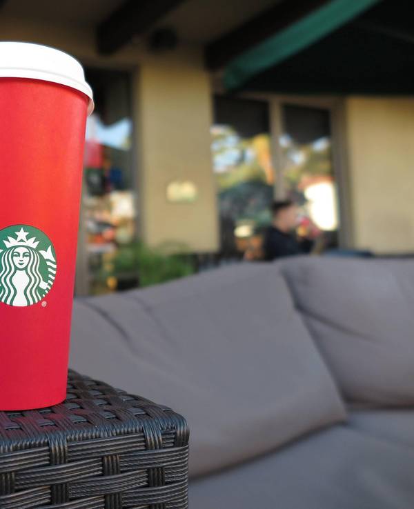 Ein roter To-go-Becher von Starbucks steht auf der Armlehne einer Couch.
