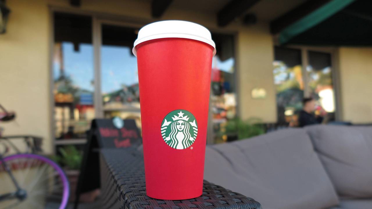 Ein roter To-go-Becher von Starbucks steht auf der Armlehne einer Couch.