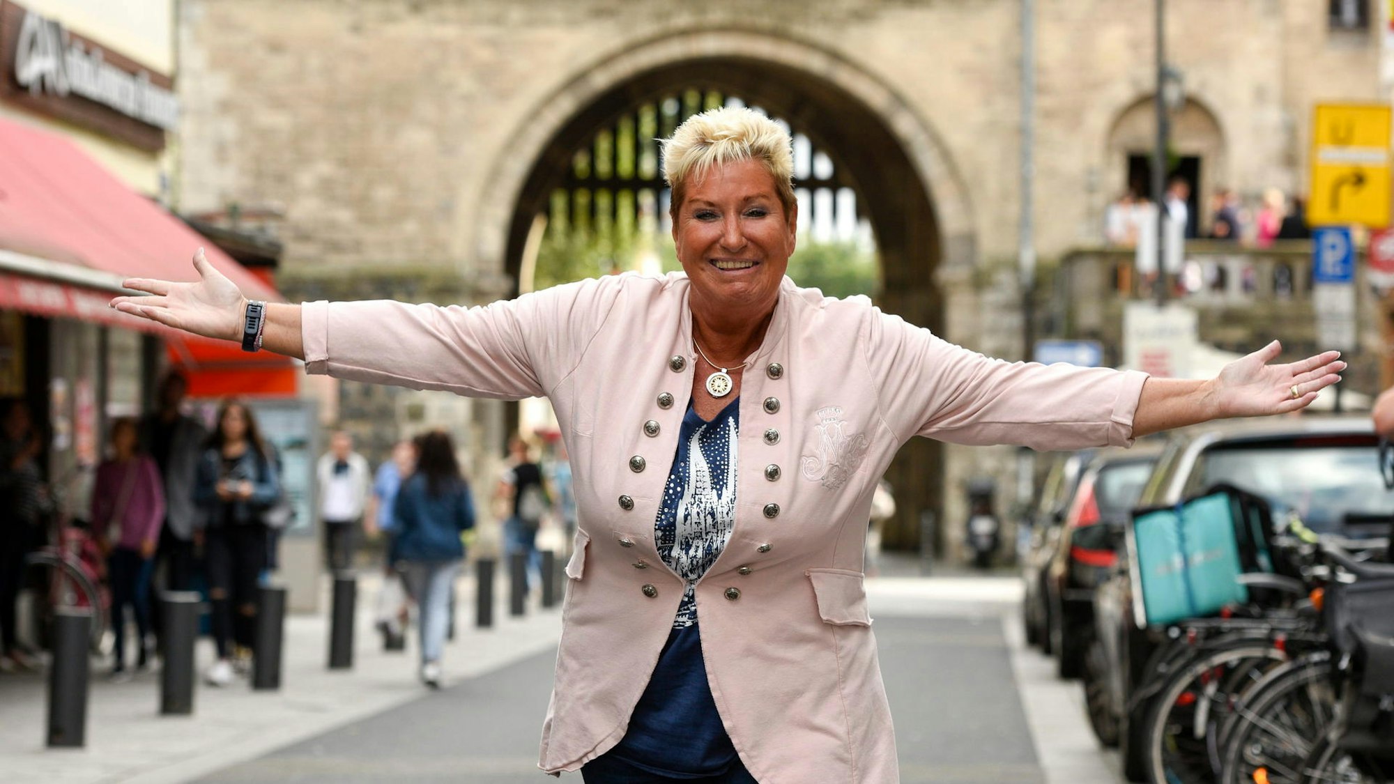 Marita Köllner steht mit ausgebreiteten Armen auf der Severinstraße