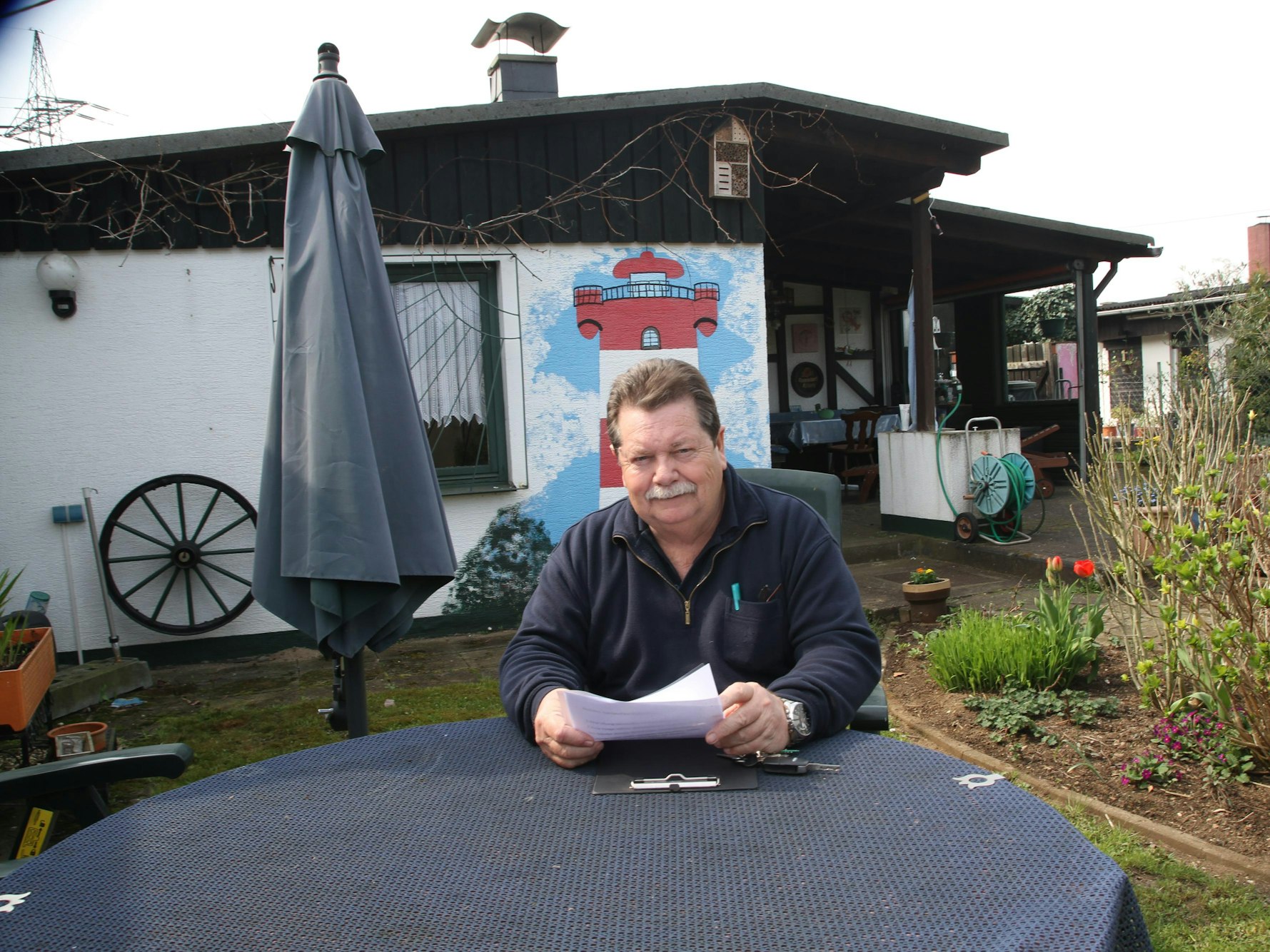 Hans Gilson sitzt an einem Tisch in einem Kleingarten.