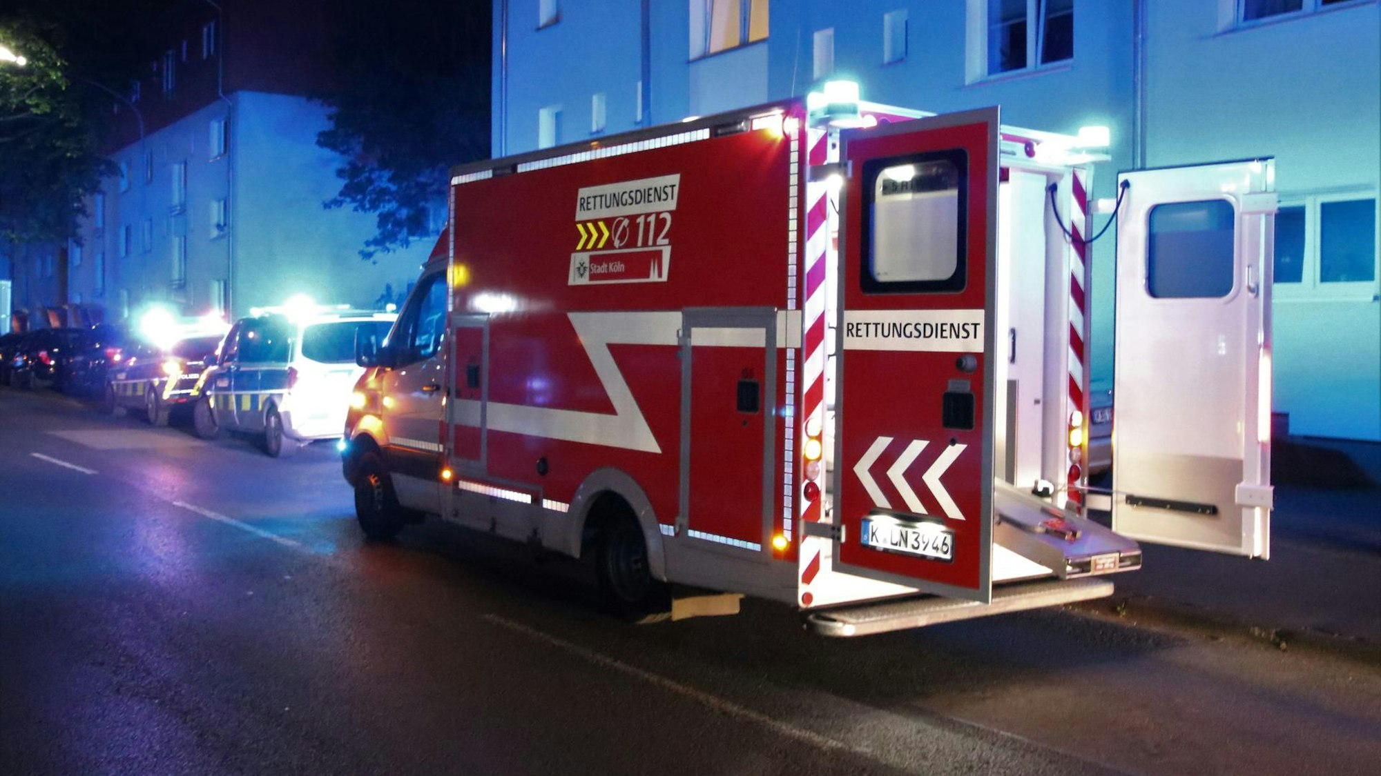 Ein Rettungswagen steht mit offenen Türen auf der Straße, davor stehen zwei Streifenwagen der Polizei.