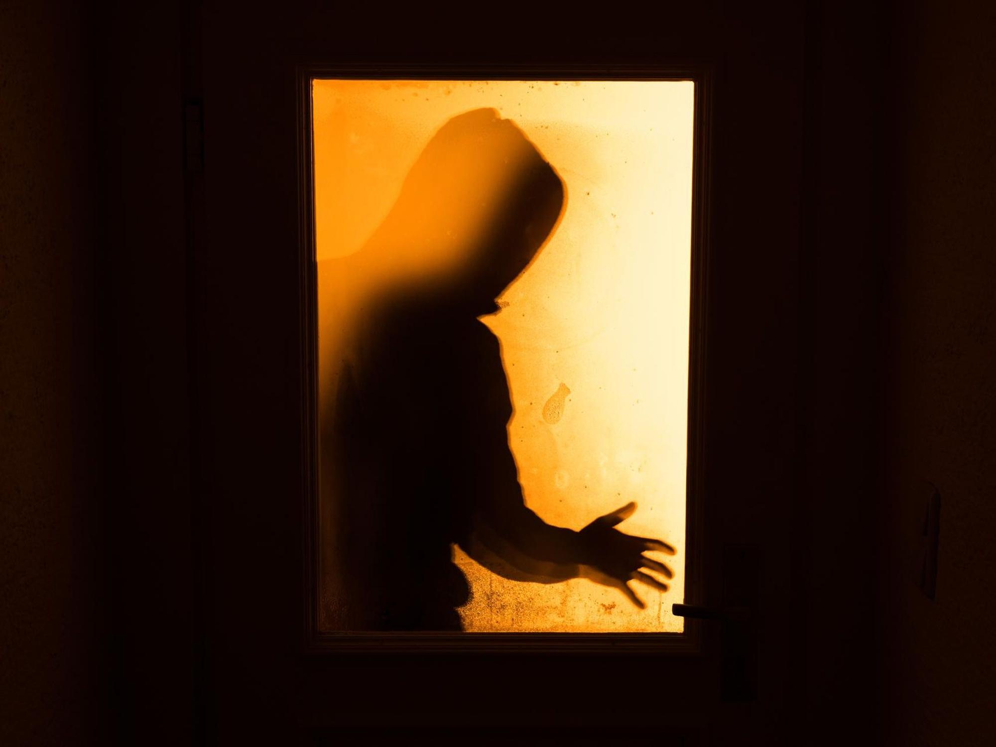 Der Schatten eines Mannes, der hinter einer gläsernen Wohnungstür zu sehen ist.
