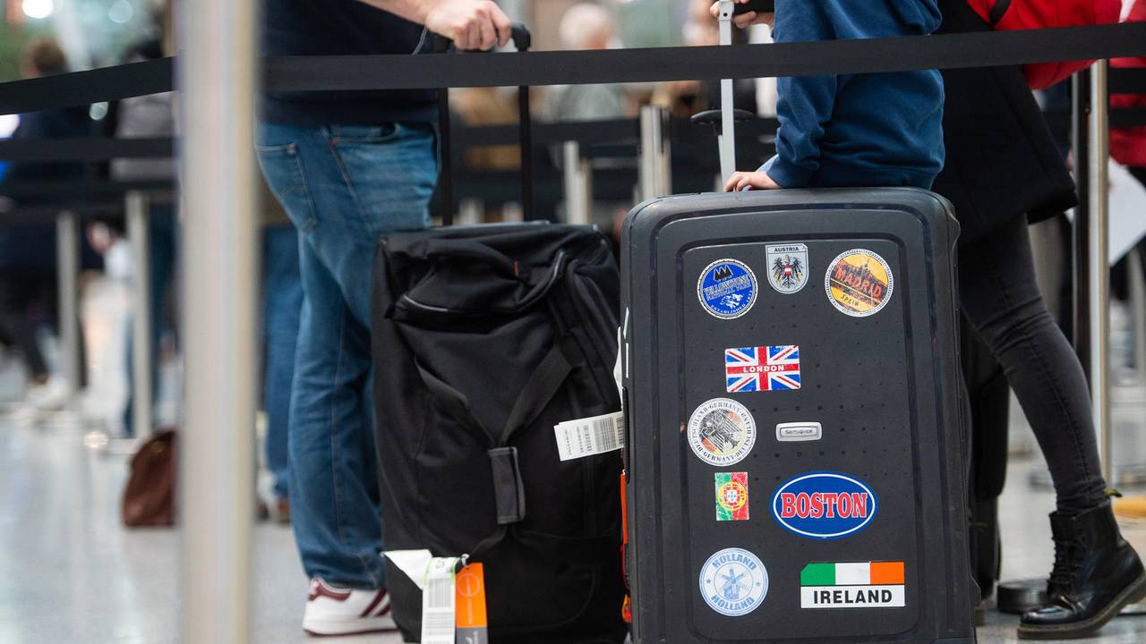 Reisende stehen in einem Flughafen einer Schlange mit ihrem Gepäck.