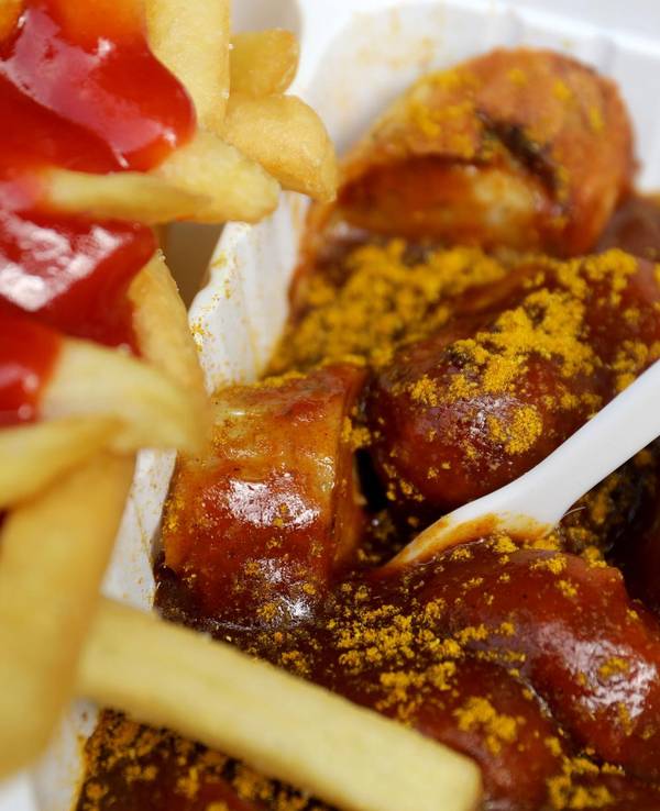 Das undatierte Symbolfoto zeigt eine Portion Currywurst mit Pommes und Ketchup. In der Currywurst steckt eine weiße Plastikgabel.