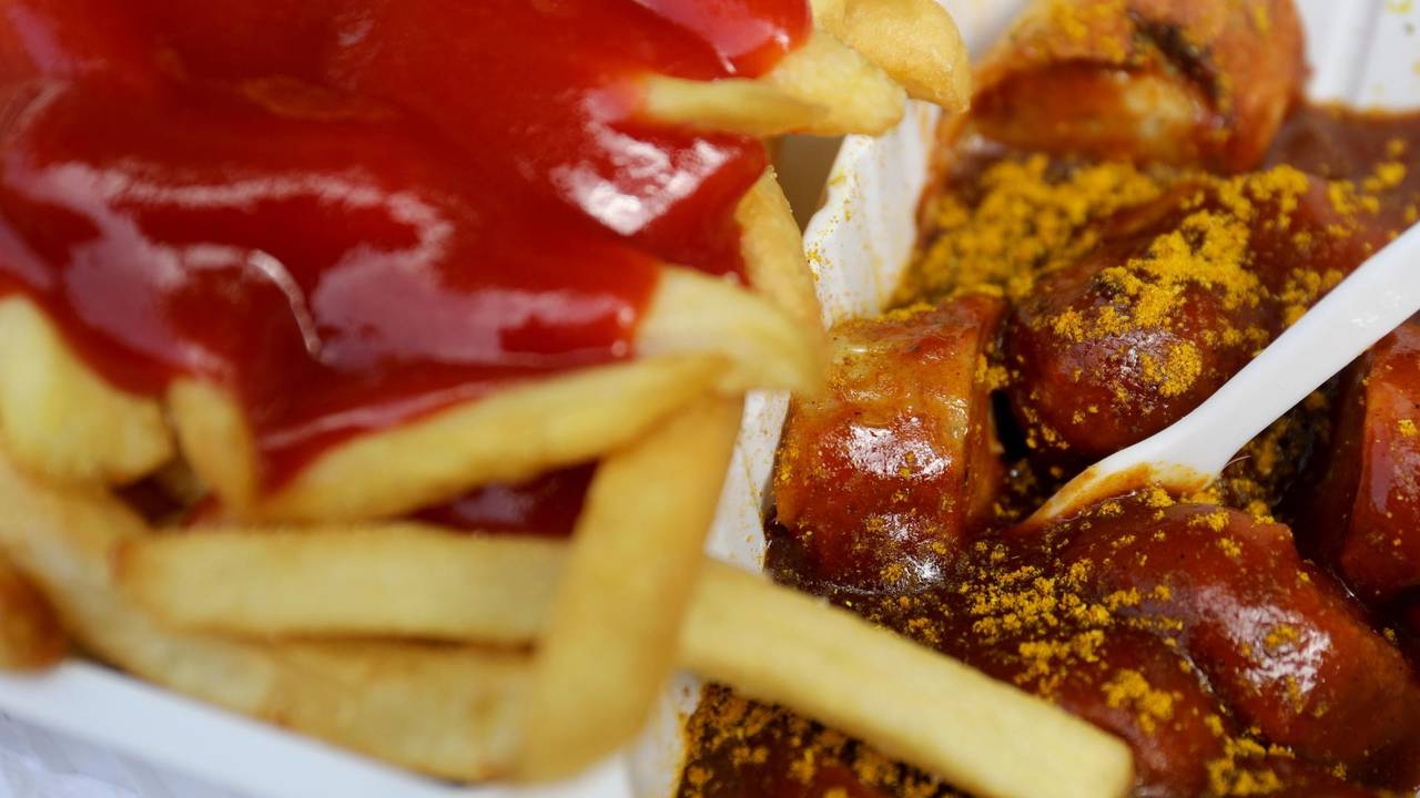 Das undatierte Symbolfoto zeigt eine Portion Currywurst mit Pommes und Ketchup. In der Currywurst steckt eine weiße Plastikgabel.