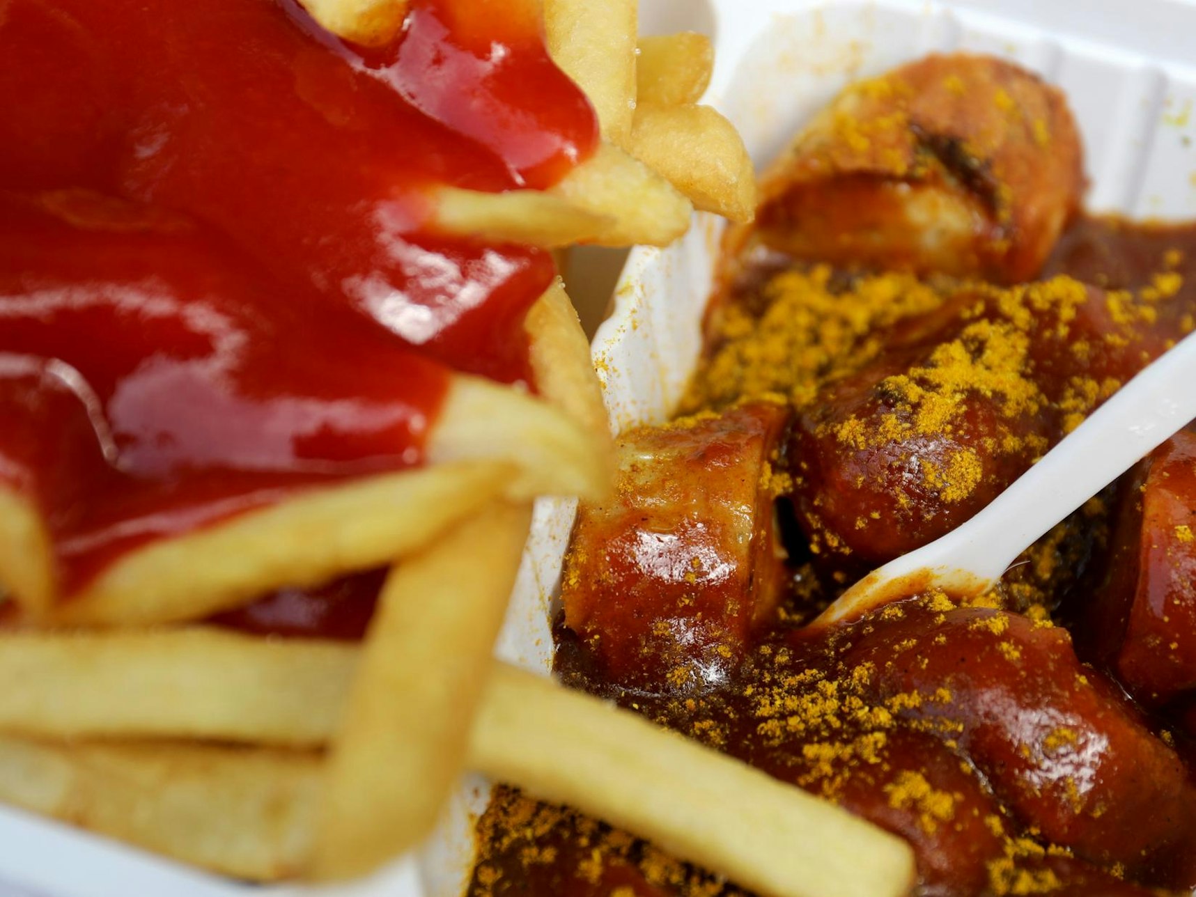 Das undatierte Symbolfoto zeigt eine Portion Currywurst mit Pommes und Ketchup. In der Currywurst steckt eine weiße Plastikgabel.