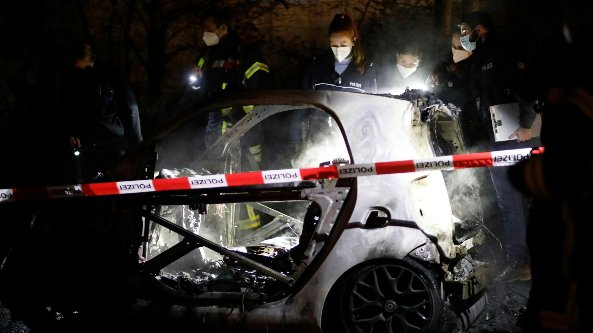 Ermittler stehen an einem ausgebrannten Smart.