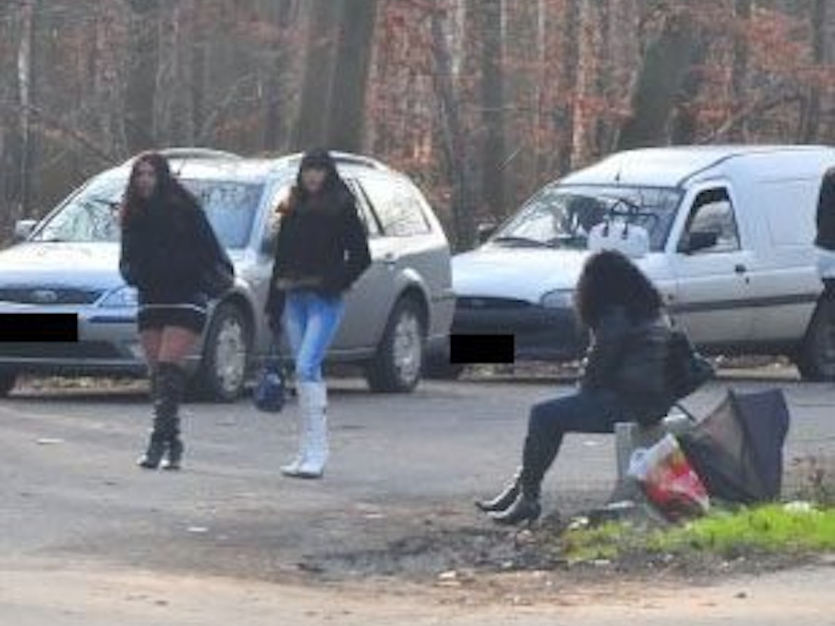 Eine Frau sitzt am Straßenstrich, zwei weitere gehen an ihr vorbei.