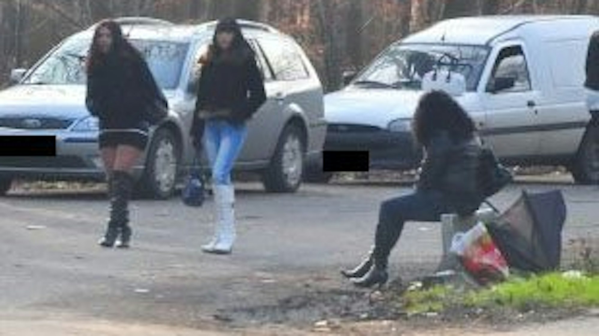 Eine Frau sitzt am Straßenstrich, zwei weitere gehen an ihr vorbei.