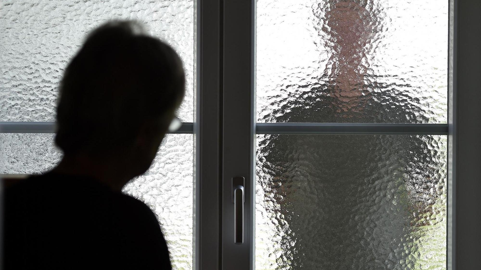 Eine Frau sieht durch die Scheibe einer Tür die Silhouette einer Person.