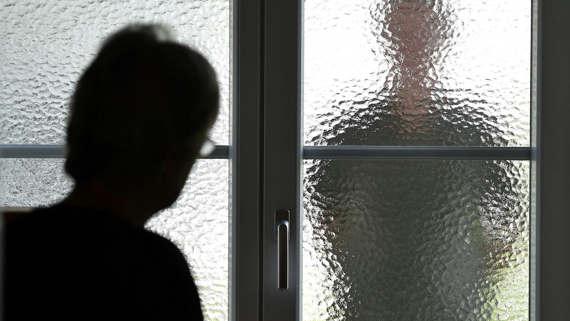 Eine Frau sieht durch die Scheibe einer Tür die Silhouette einer Person.