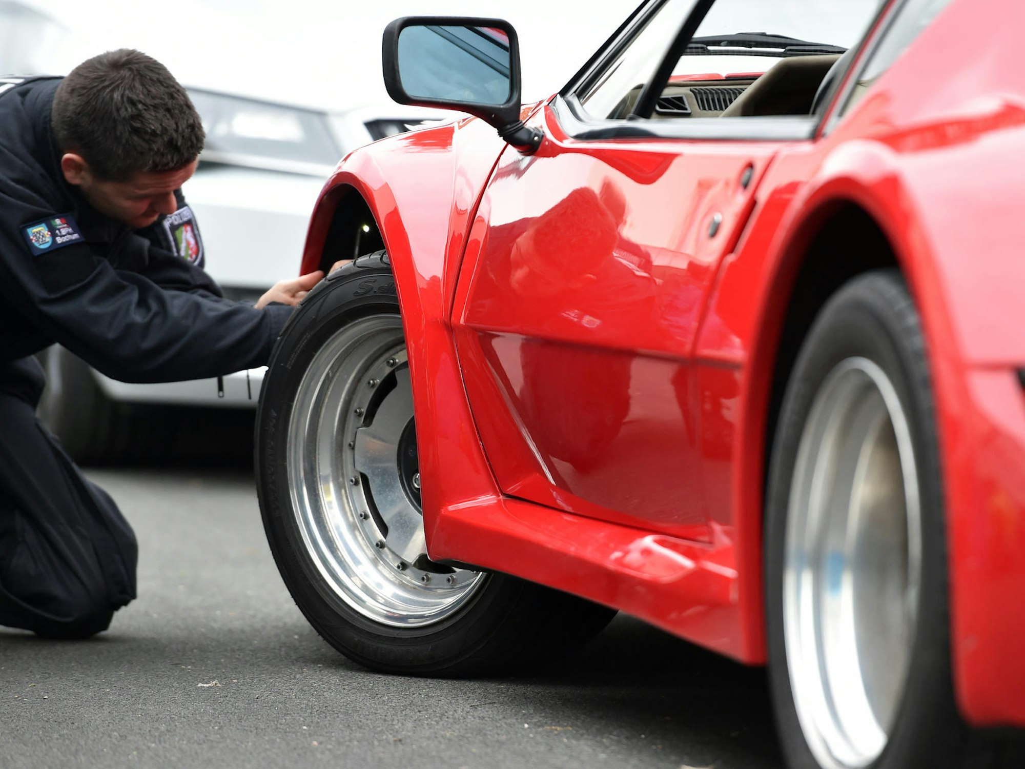Ein Polizist überprüft knieend einen getunten Sportwagen.
