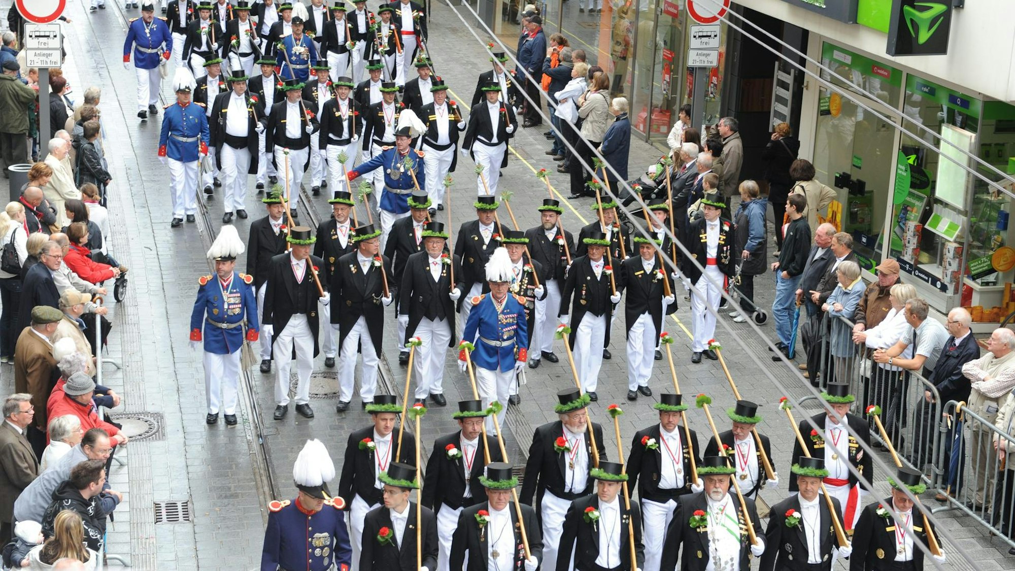 Die Neusser Bürger-Schützen marschieren über eine Straße, die von Schaulustigen gesäumt ist.