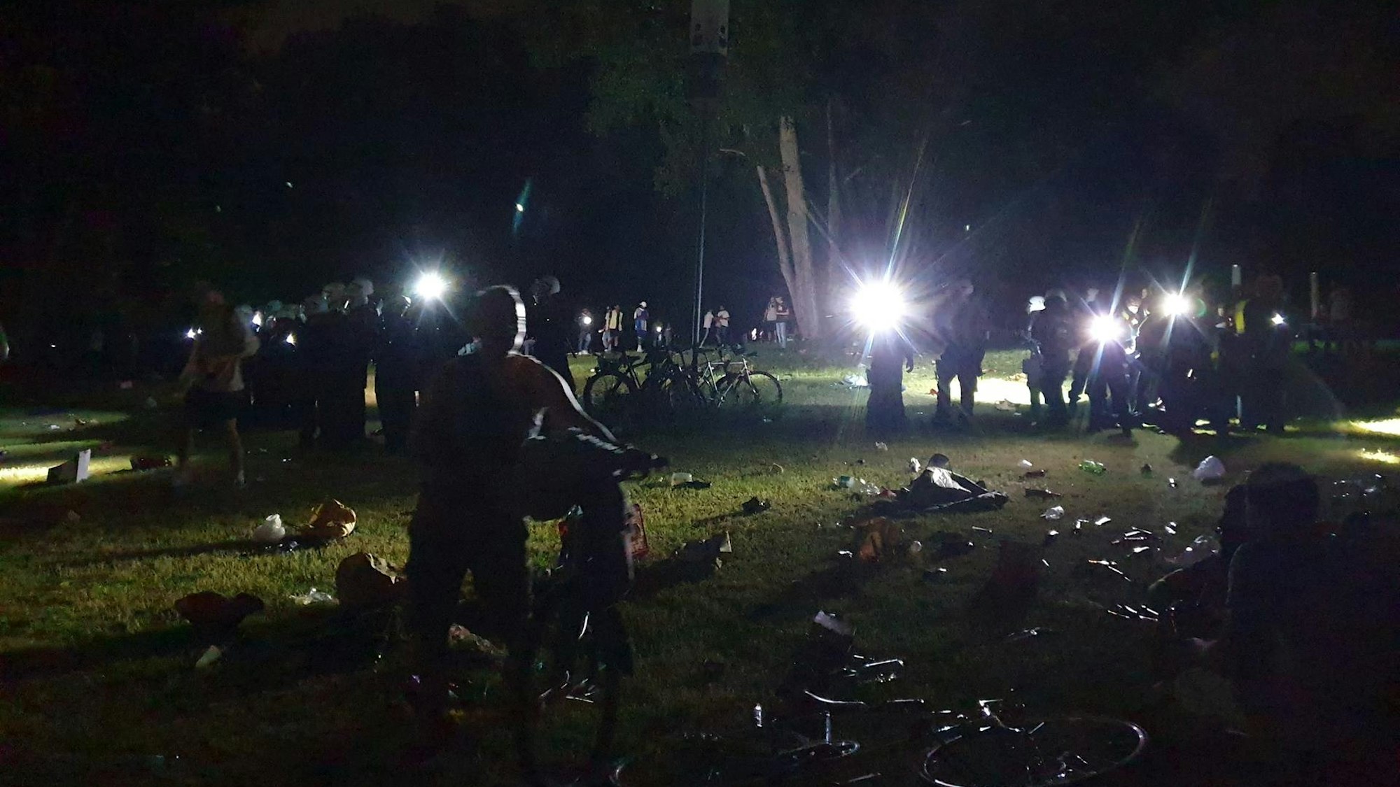 Kölner Polizisten leuchten mit Taschenlampen über die Wiese am Aachener Weiher
