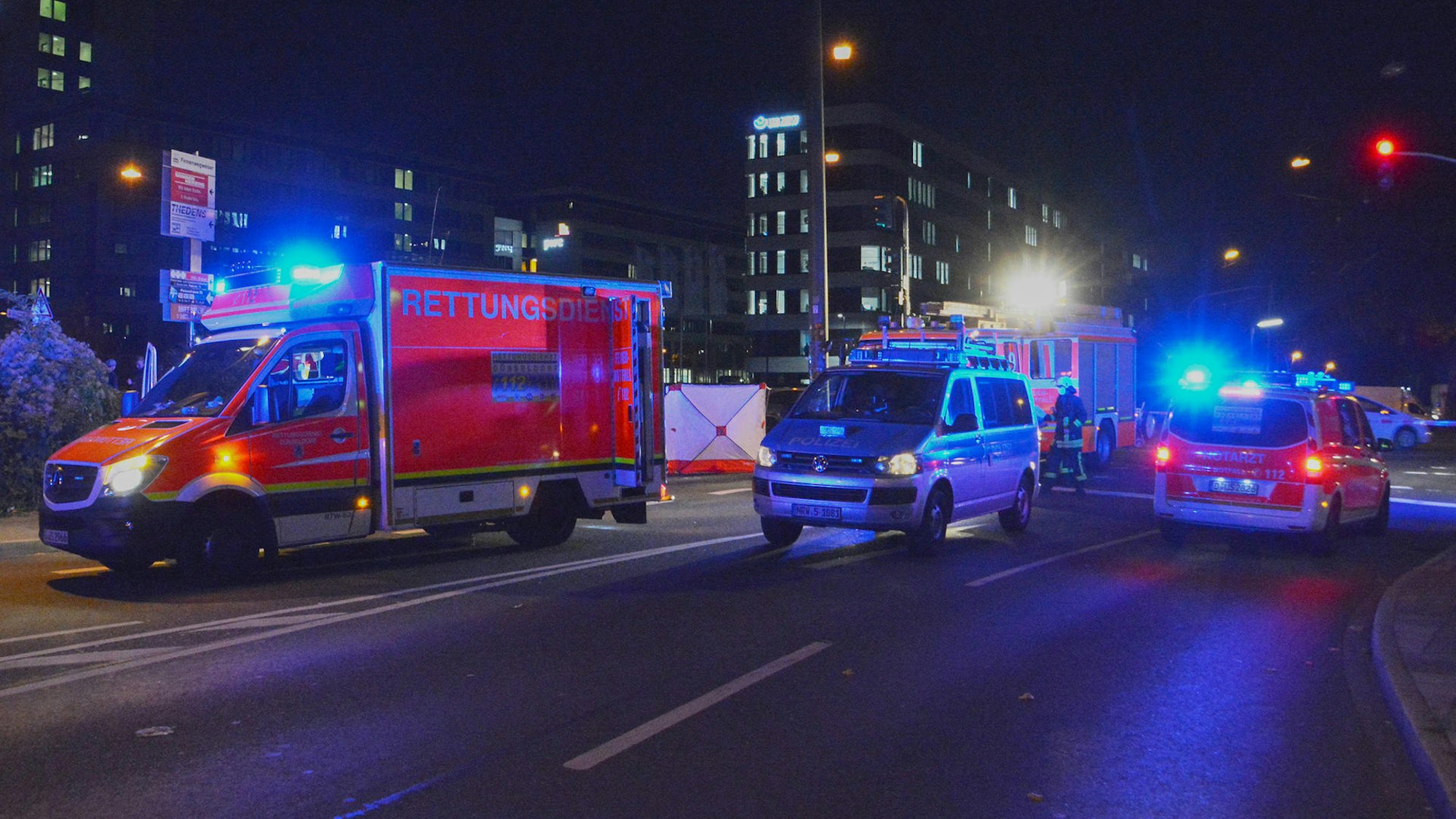 Ein Rettungswagen sowie Einsatzfahrzeuge von Polizei und Feuerwehr stehen bei Nacht auf einer Straße, auf der ein Unfall passiert ist.