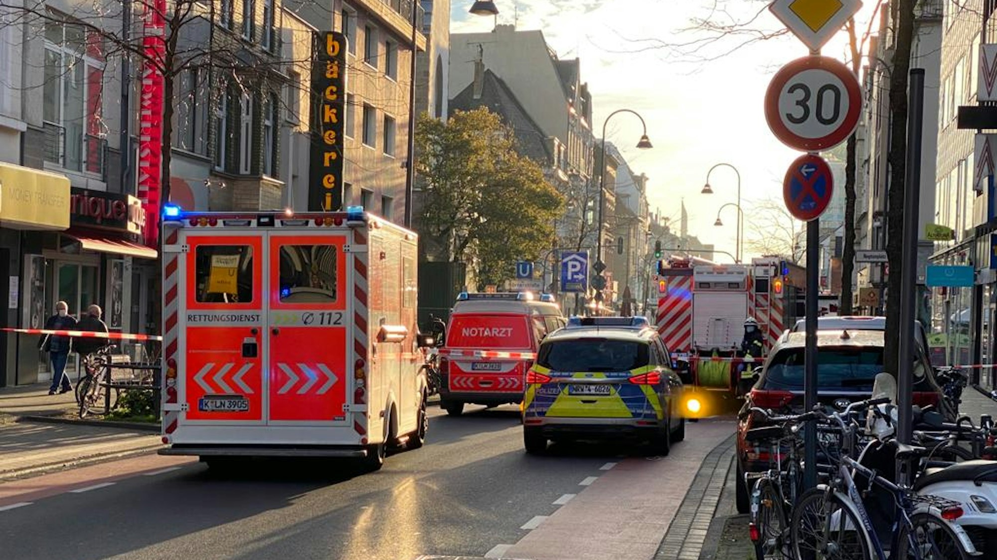 Die Polizei hat die Fahrbahn einer Straße abgesperrt, mehrere Einsatzfahrzeuge von Polizei, Rettungsdienst und Feuerwehr sind vor Ort.