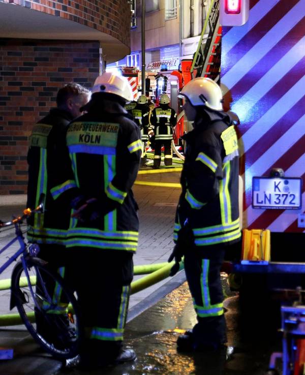 Drei Feuerwehrleute stehen nachts an einem Löschfahrzeug.