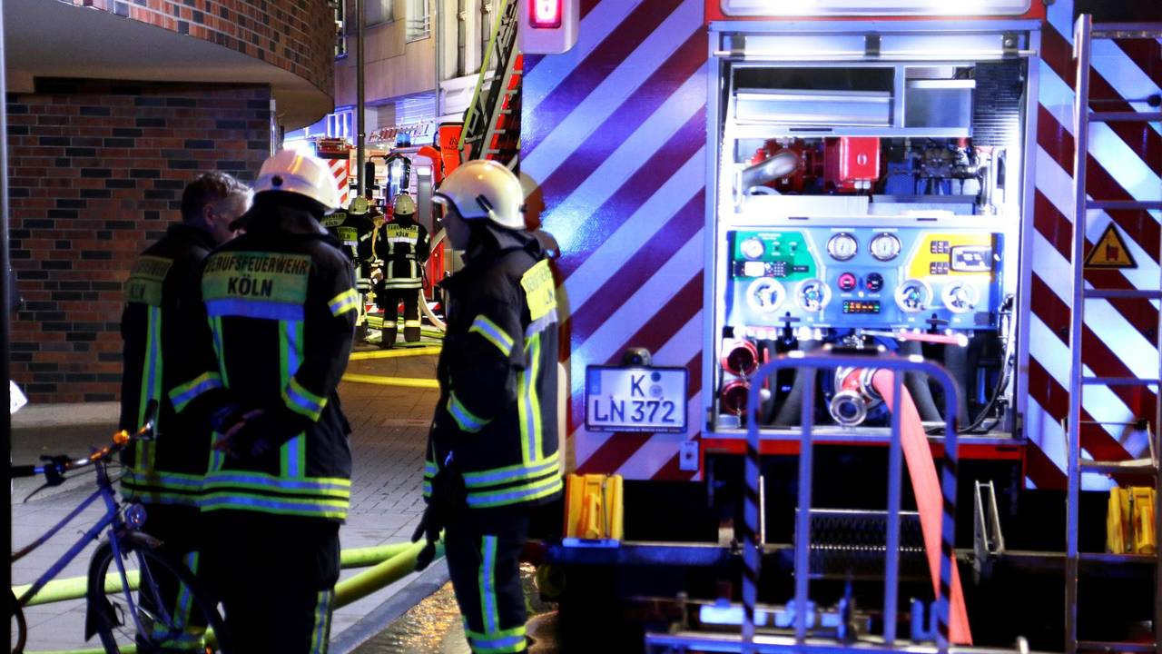 Drei Feuerwehrleute stehen nachts an einem Löschfahrzeug.