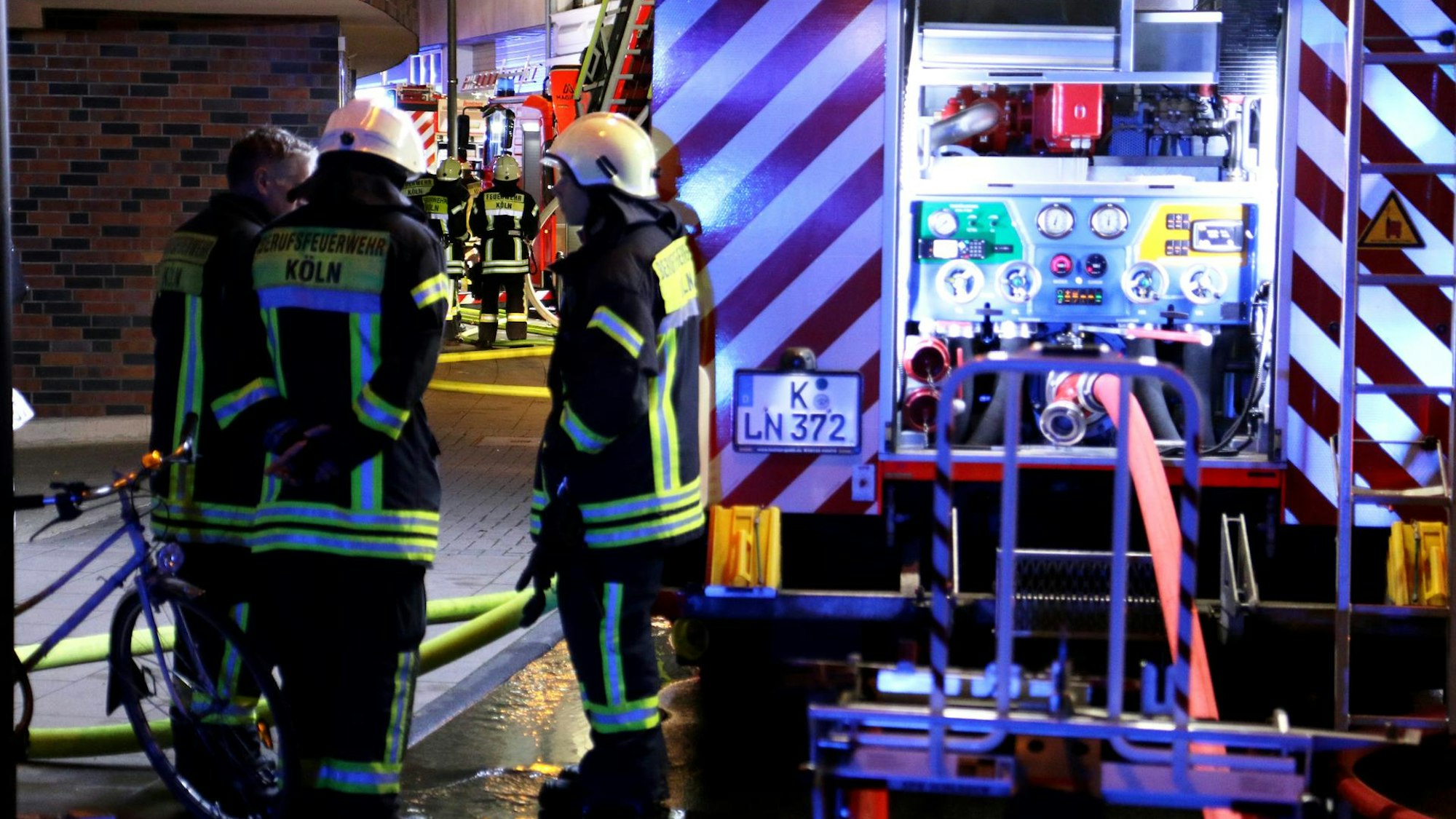 Einsatzkräfte der Kölner Feuerwehr stehen neben einem Löschfahrzeug.