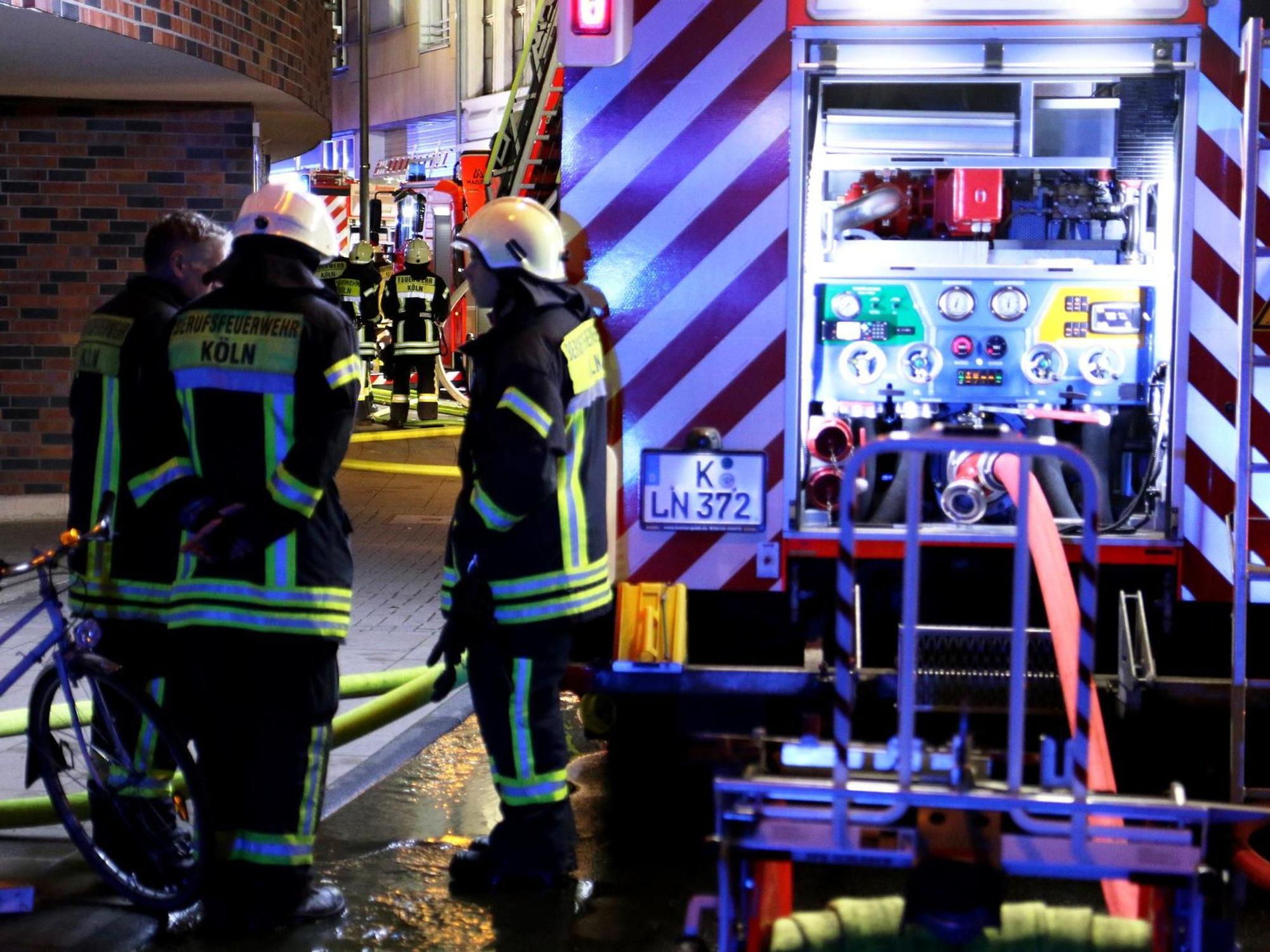 Drei Feuerwehrleute stehen nachts an einem Löschfahrzeug.