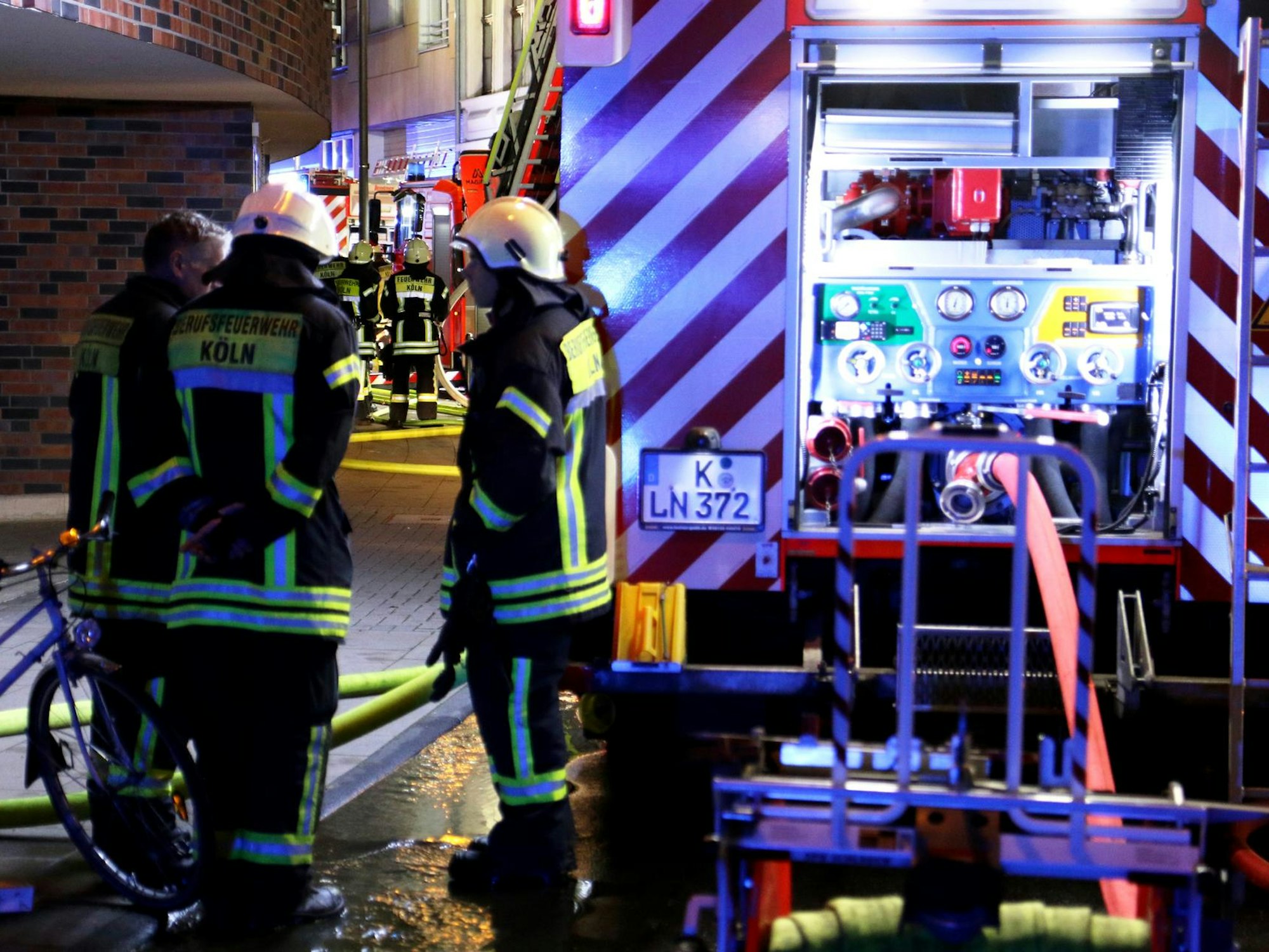 Drei Feuerwehrleute stehen nachts an einem Löschfahrzeug.