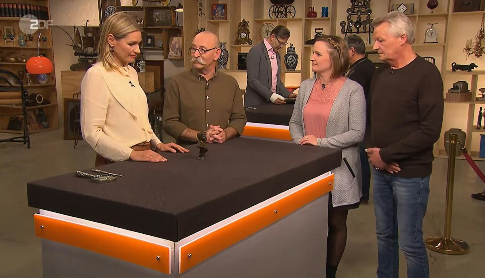 Bianca Berding begutachtet ein Kunstwerk bei Bares für Rares. Neben ihr steht Moderator Horst Lichter sowie die Verkäuferin.