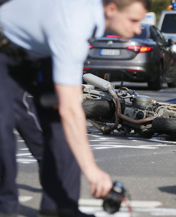 Ein Polizist markiert auf einer Fahrbahn Spuren, im Hintergrund liegt ein verunglücktes Motorrad.