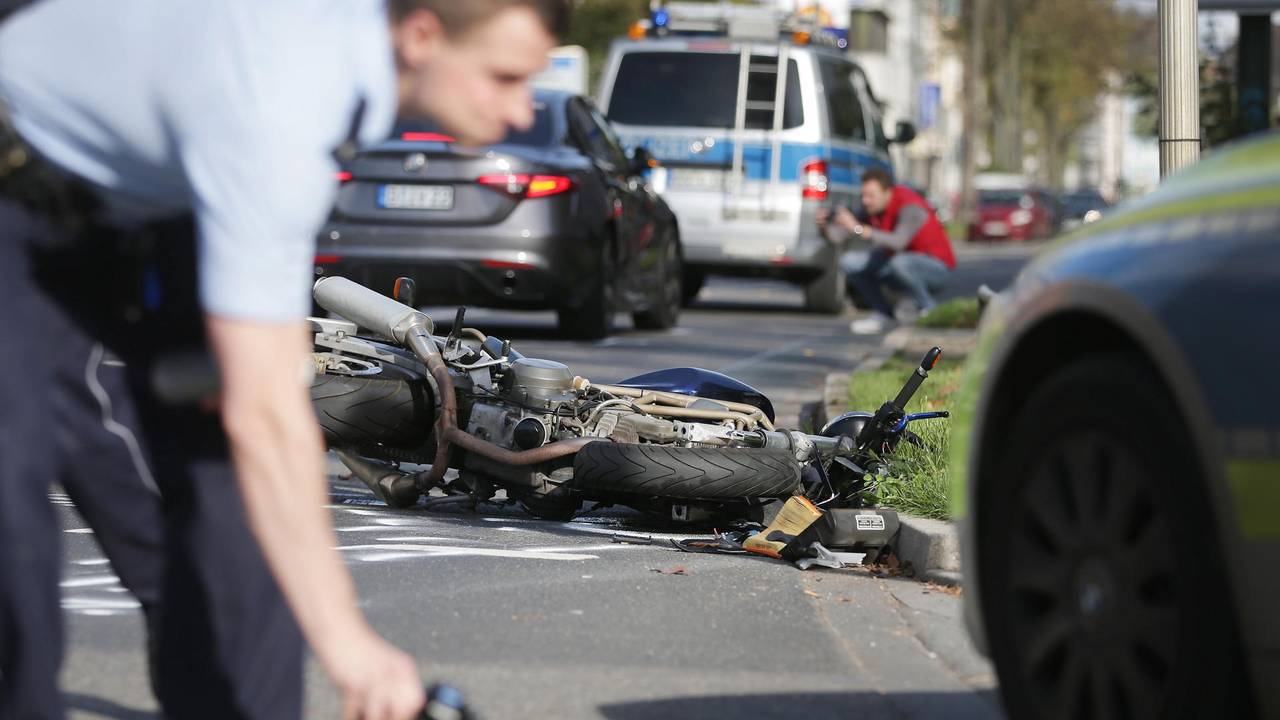 Ein Polizist markiert auf einer Fahrbahn Spuren, im Hintergrund liegt ein verunglücktes Motorrad.