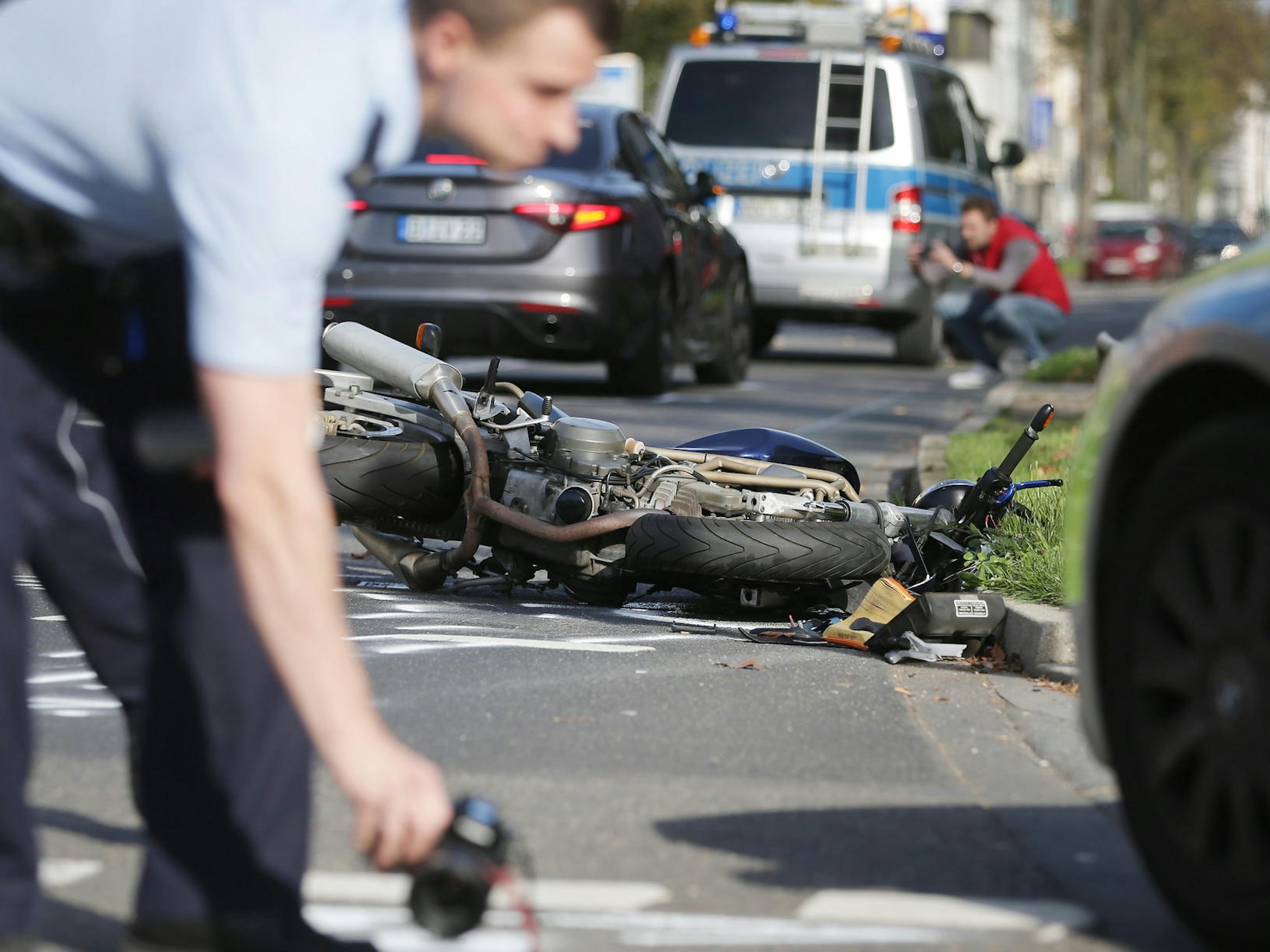 Ein Polizist markiert auf einer Fahrbahn Spuren, im Hintergrund liegt ein verunglücktes Motorrad.