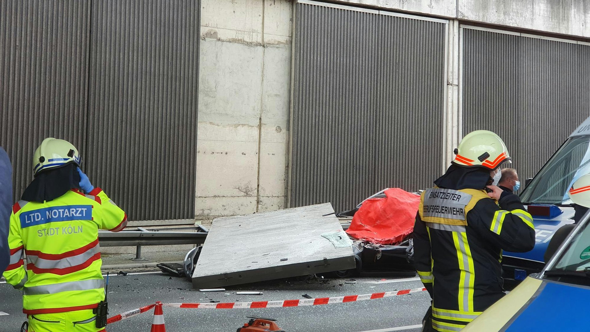 Eine Betonplatte hat ein Auto unter sich begraben, ein Notarzt und ein Feuerwehrmann stehen davor.
