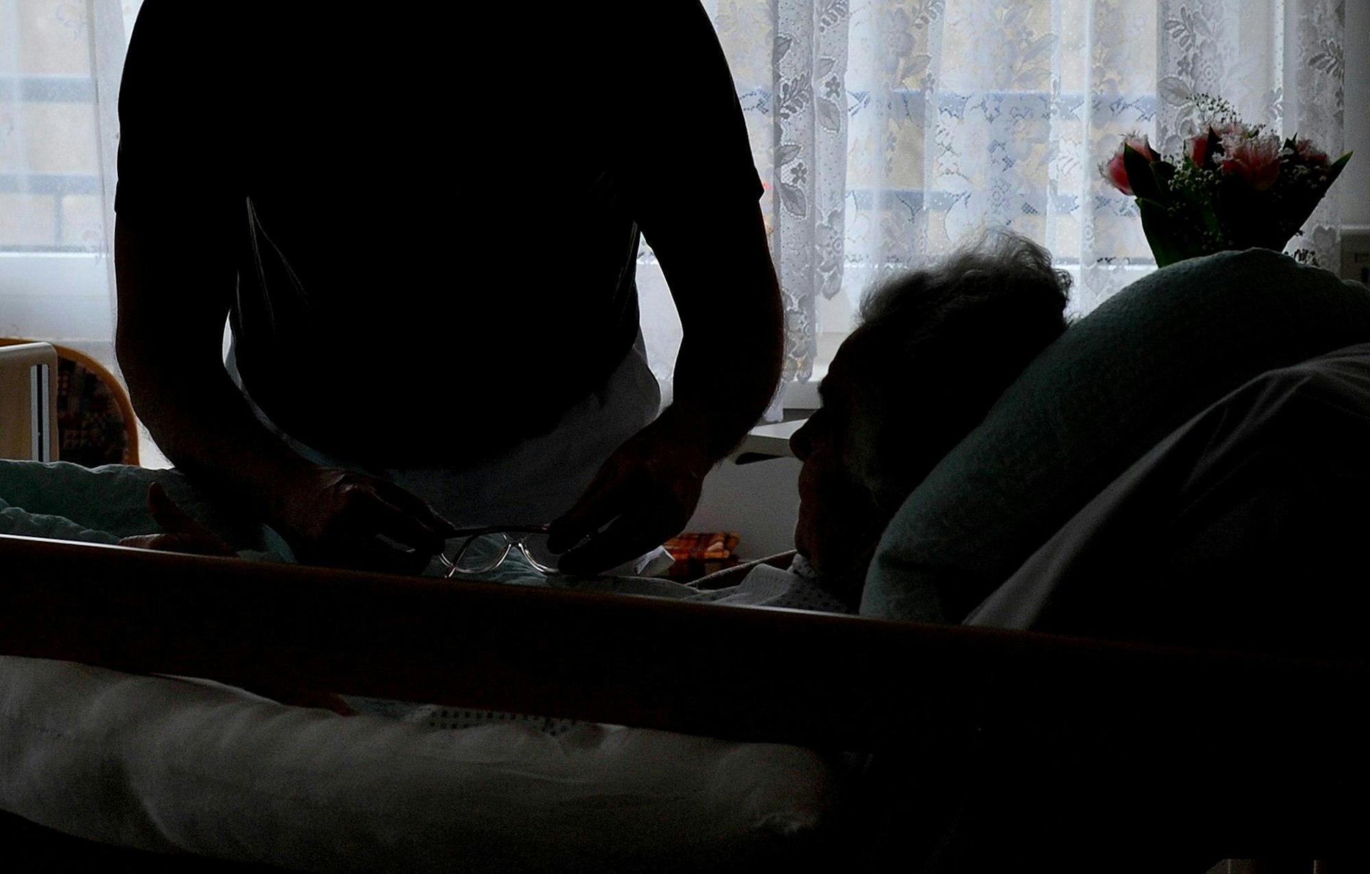 Ein Pfleger hilft einer im Bett liegenden Frau.