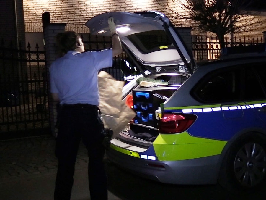 Ein Polizist verlädt eine Papiertüte im Kofferraum eines Polizeiwagens.