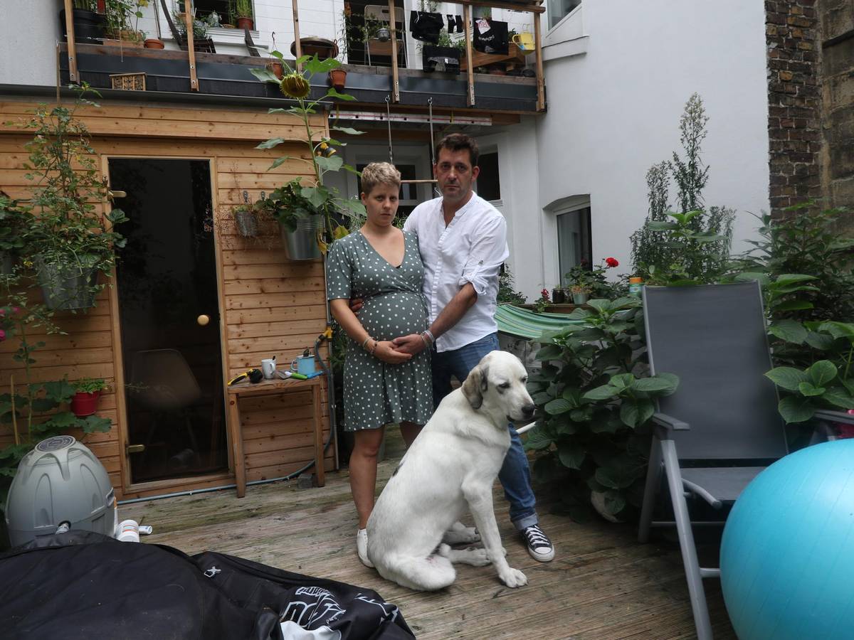 Eine schwangere Frau steht mit einem Mann und Hund auf einer Terrasse.