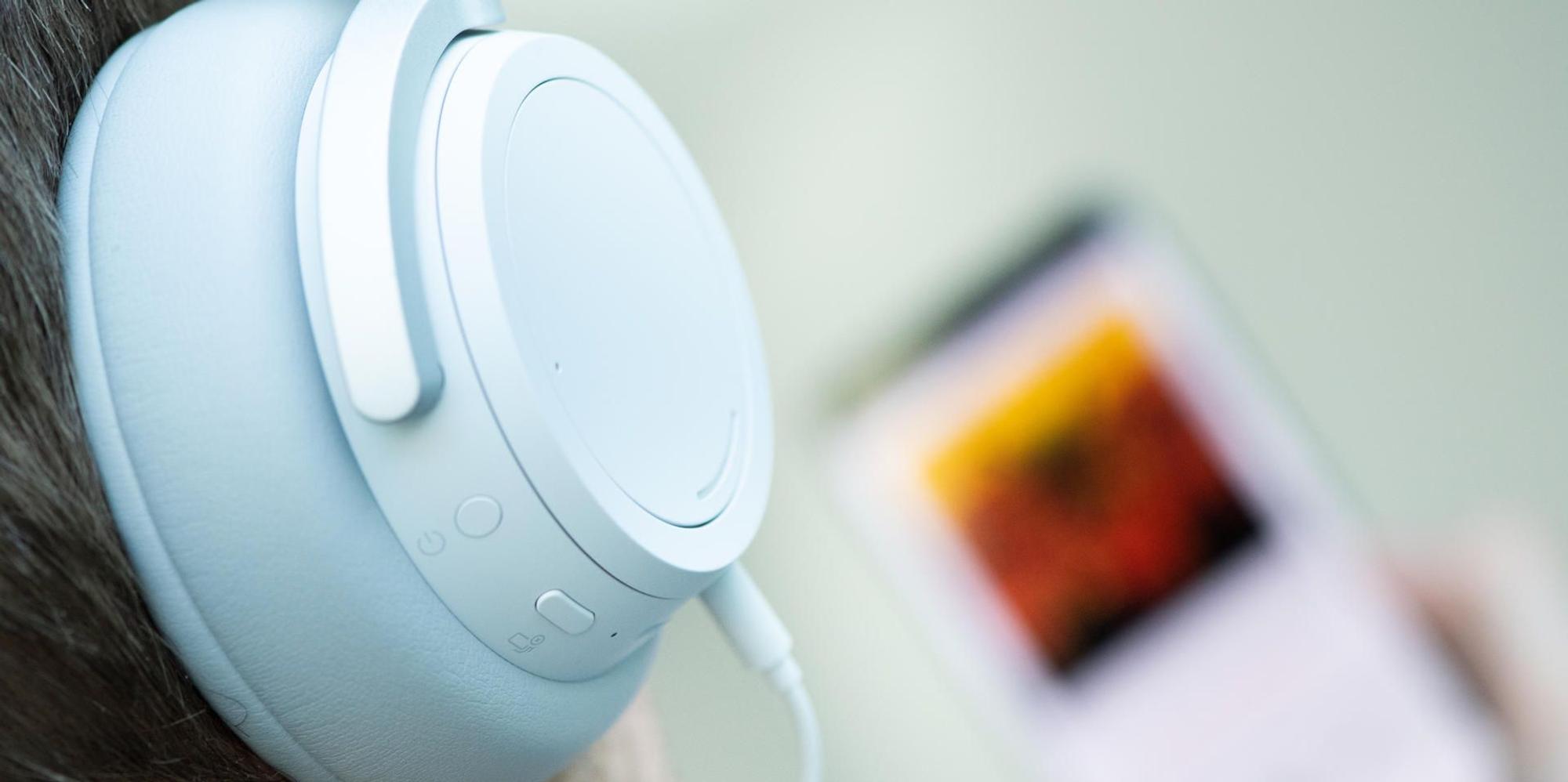 Weißer Over-Ear-Kopfhörer, im Hintergrund unscharf ein Smartphone mit Musikstreamingdienst.