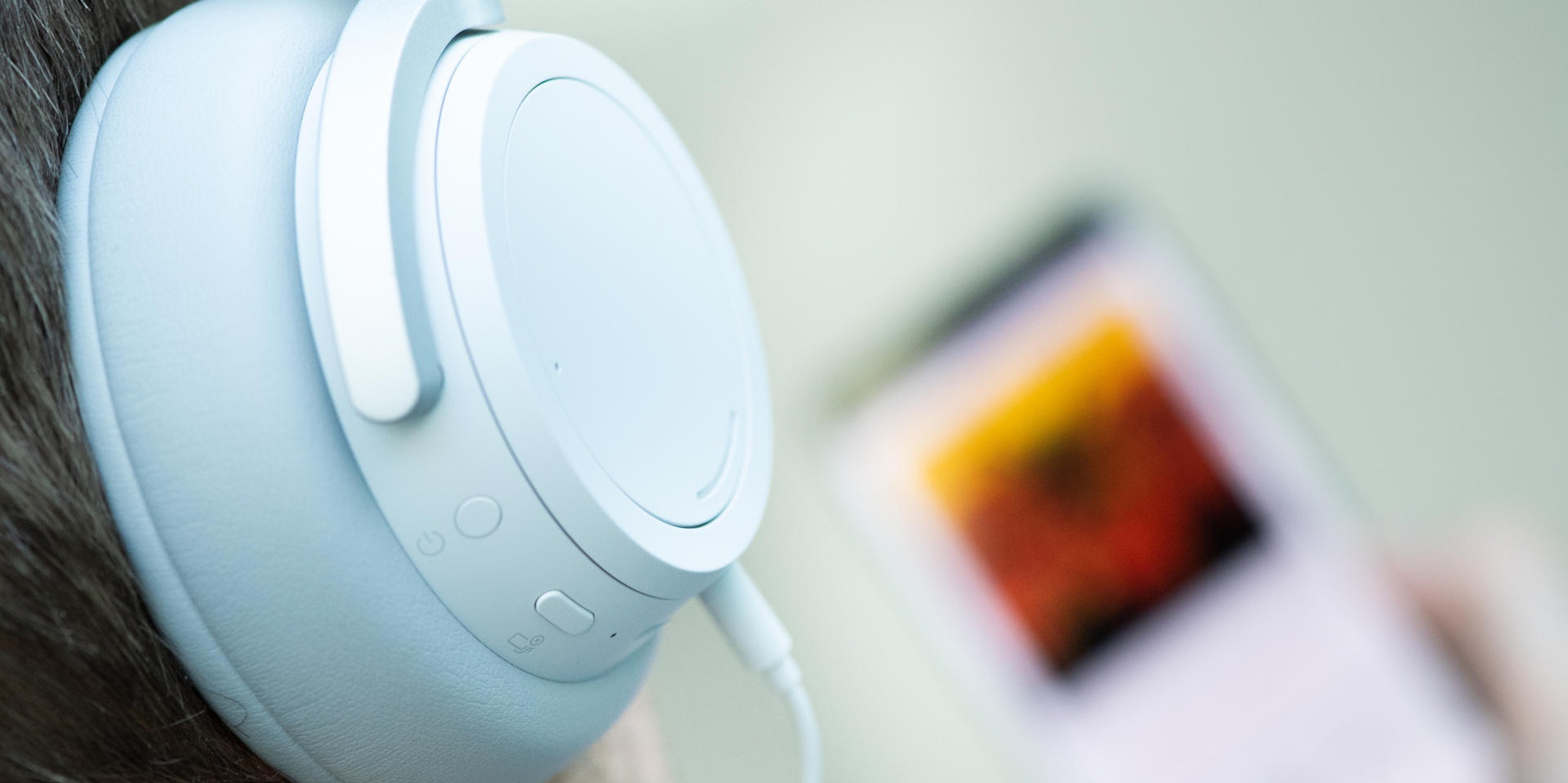 Weißer Over-Ear-Kopfhörer, im Hintergrund unscharf ein Smartphone mit Musikstreamingdienst.